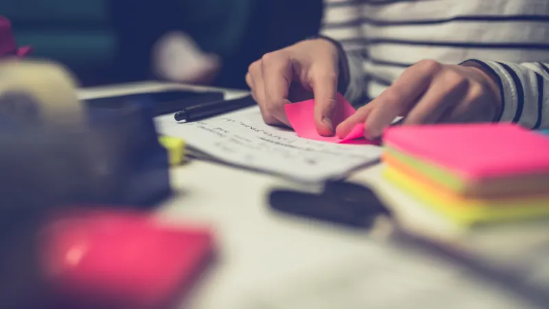 Imagem de mãos sobre mesa de escritório com post its coloridos
